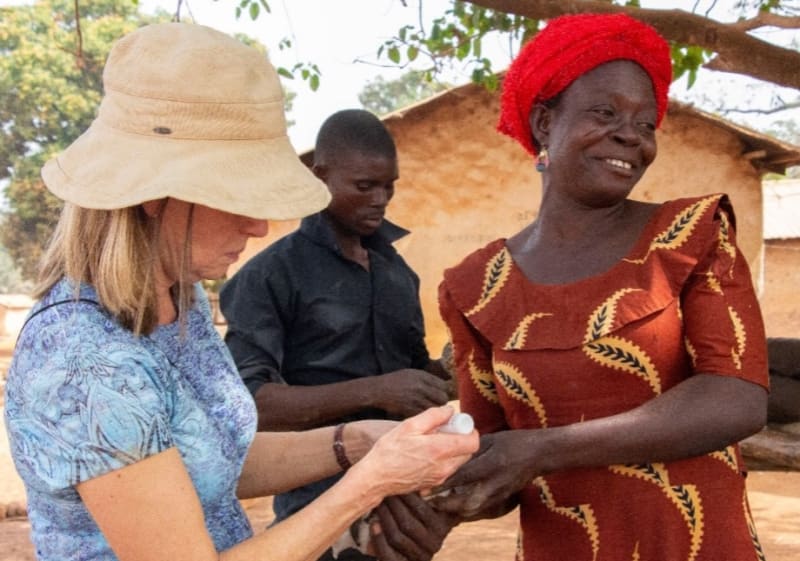 A volunteer administers drops to an unknown animal that is being held by a woman.