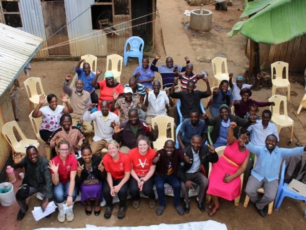 A group of Kenyan farmers with volunteers raising their hands with joy shot from above.