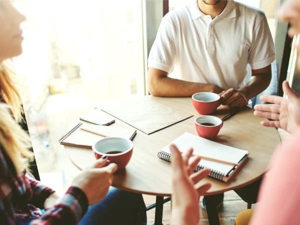 A group of people at a coffee table with cups of coffee and notepads.