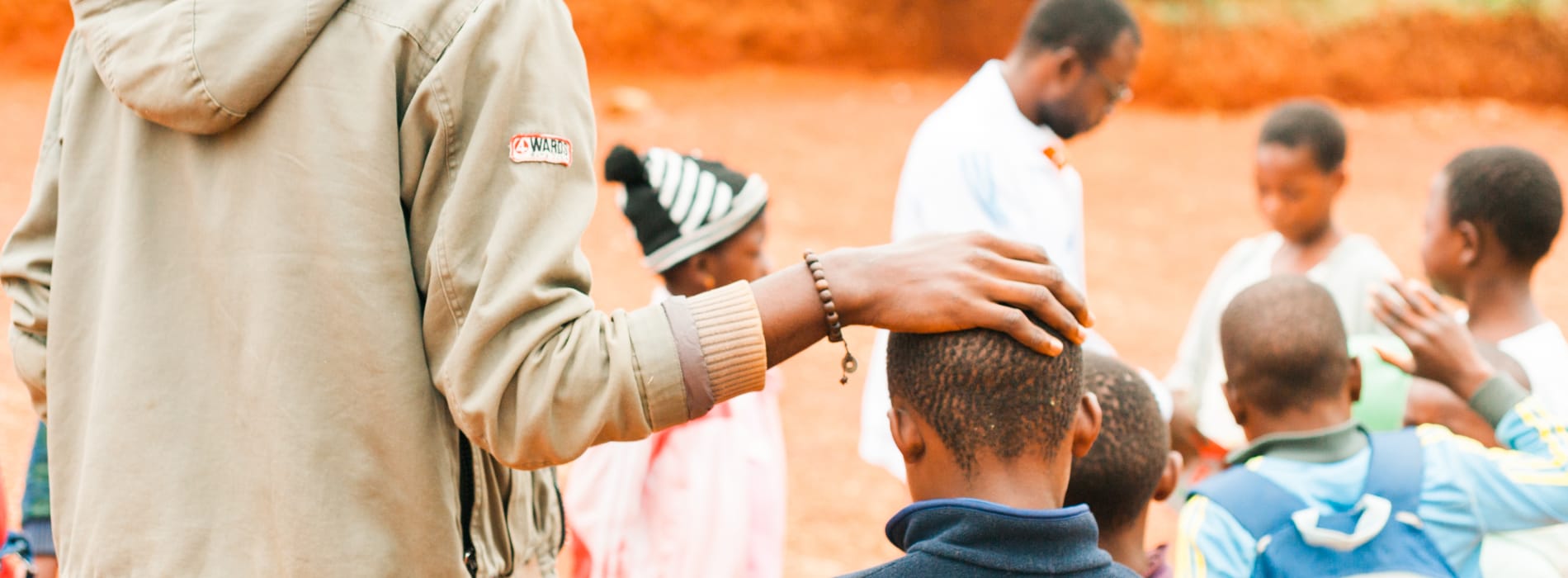 Close up from behind of a man's hand on a child's head with children standing in the background.